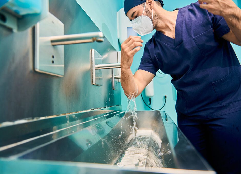 young Caucasian surgeon in scrubs washes his hands before entering the operating room in hospital. Focus on the face